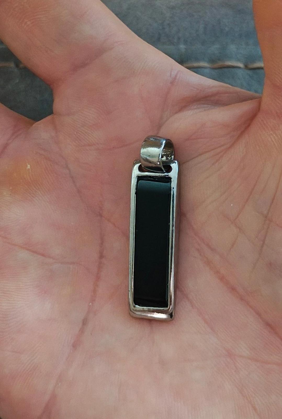 Silver-tone rectangular slide pendant held in hand, dark black inset window visible.