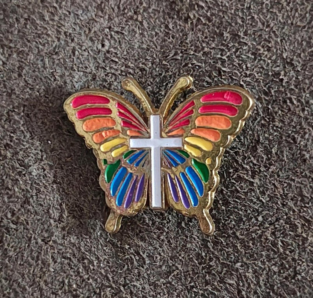 Rainbow butterfly enamel pin with multicolor wings and white cross, gold-tone frame