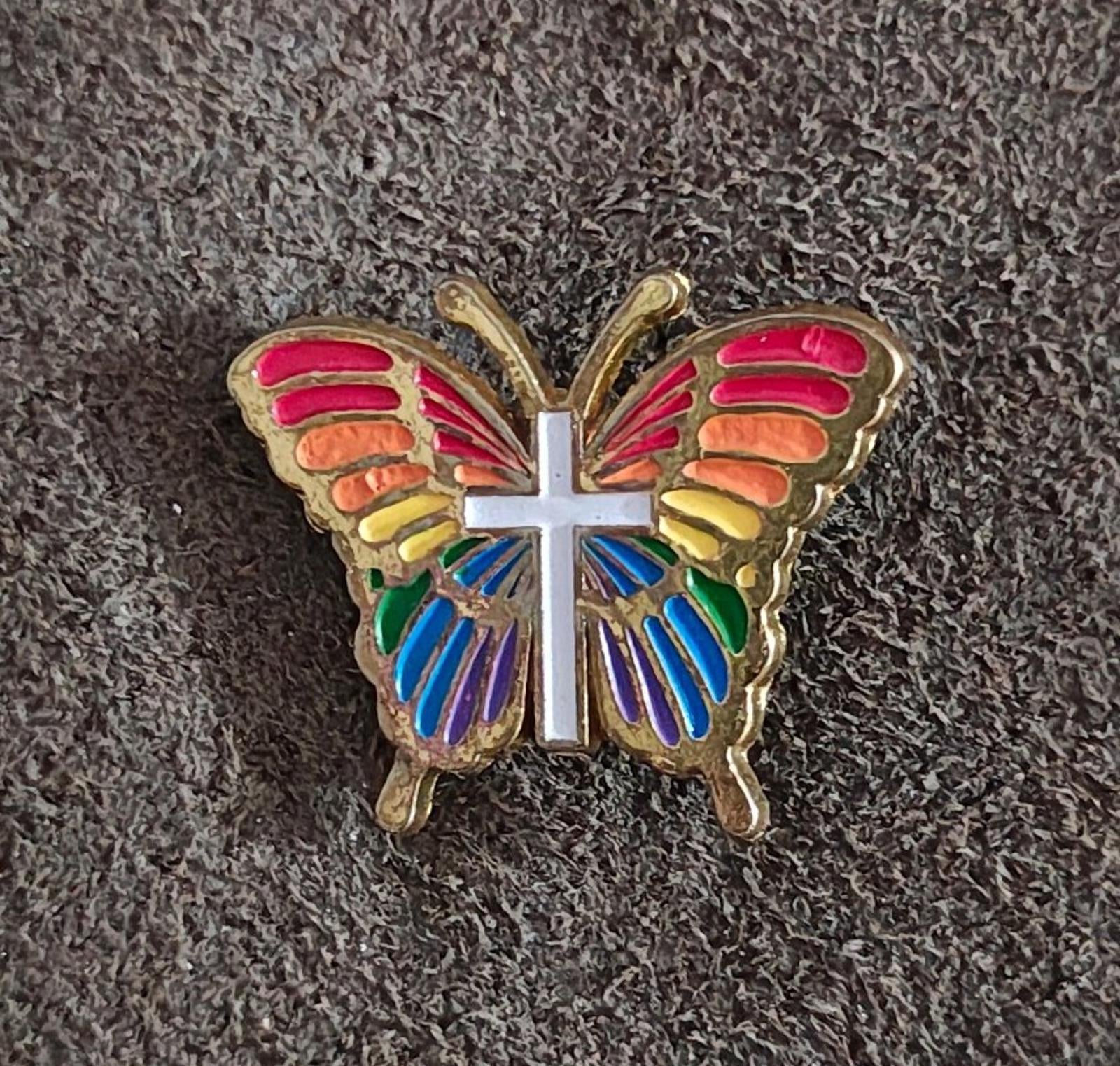 Rainbow butterfly enamel pin with multicolor wings and white cross, gold-tone frame