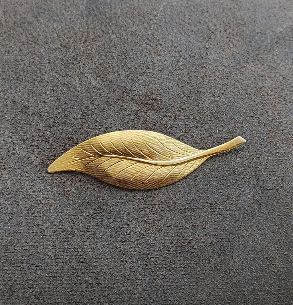 Gold-tone textured leaf brooch pin with raised veins, laid out on surface