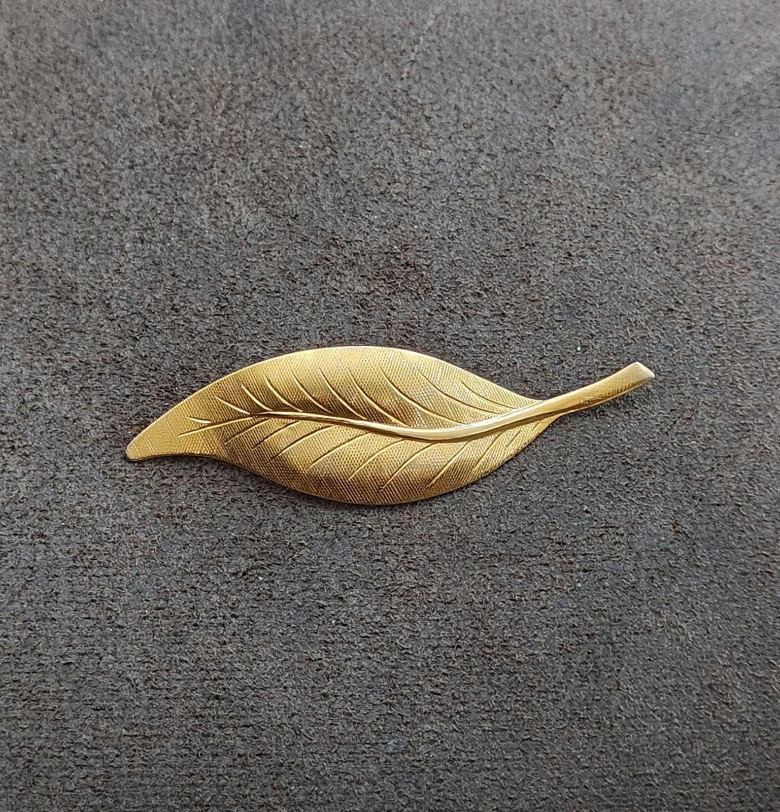 Gold-tone textured leaf brooch pin with raised veins, laid out on surface