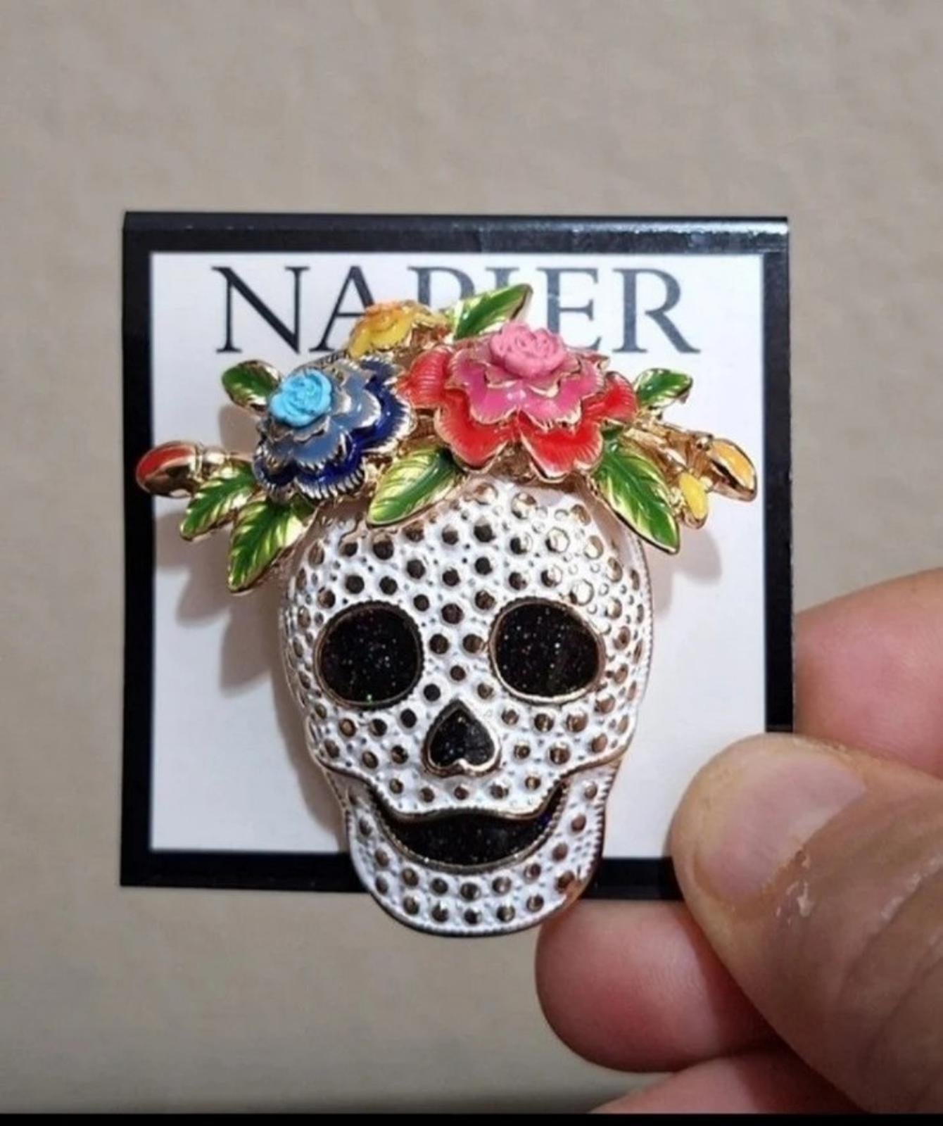Silver tone sugar skull pin with blue and pink flowers and black eyes, held by hand