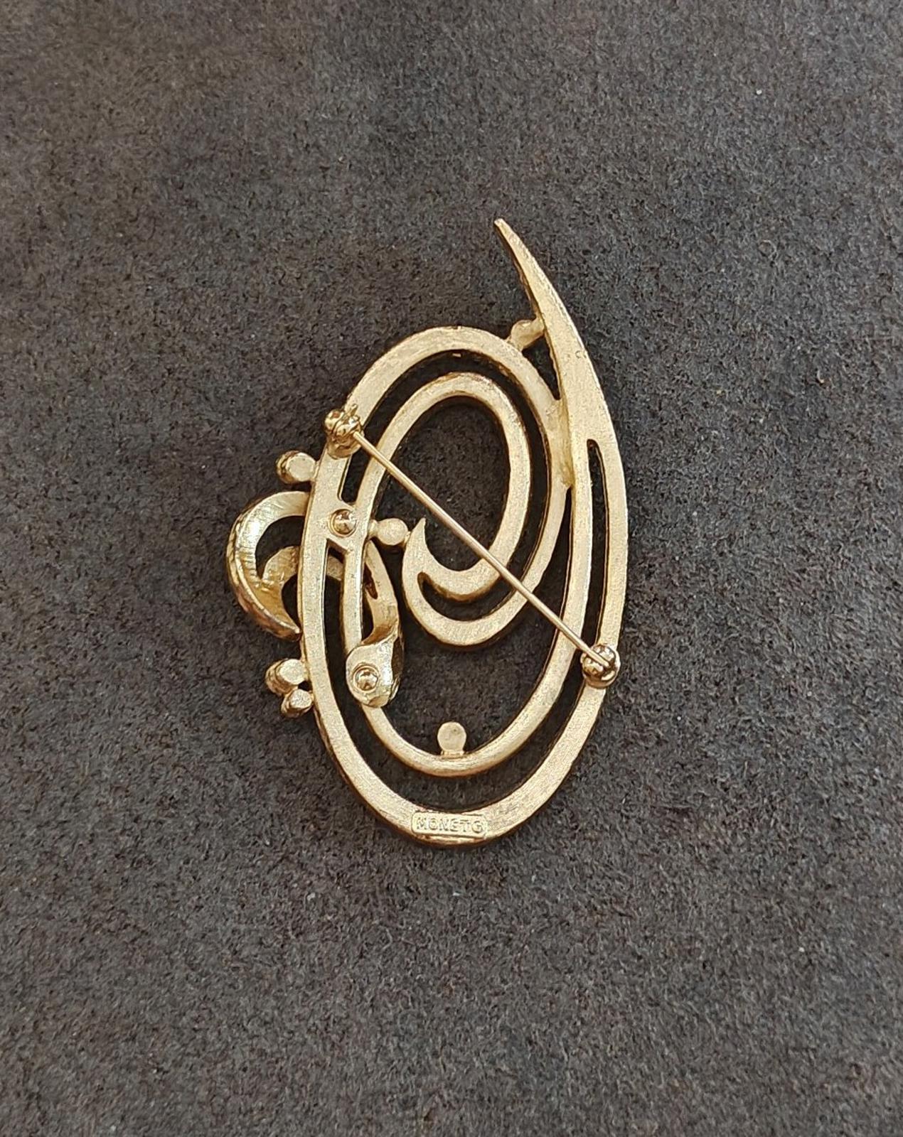 Gold tone oval brooch pin with double swirl engraving and visible pin hardware