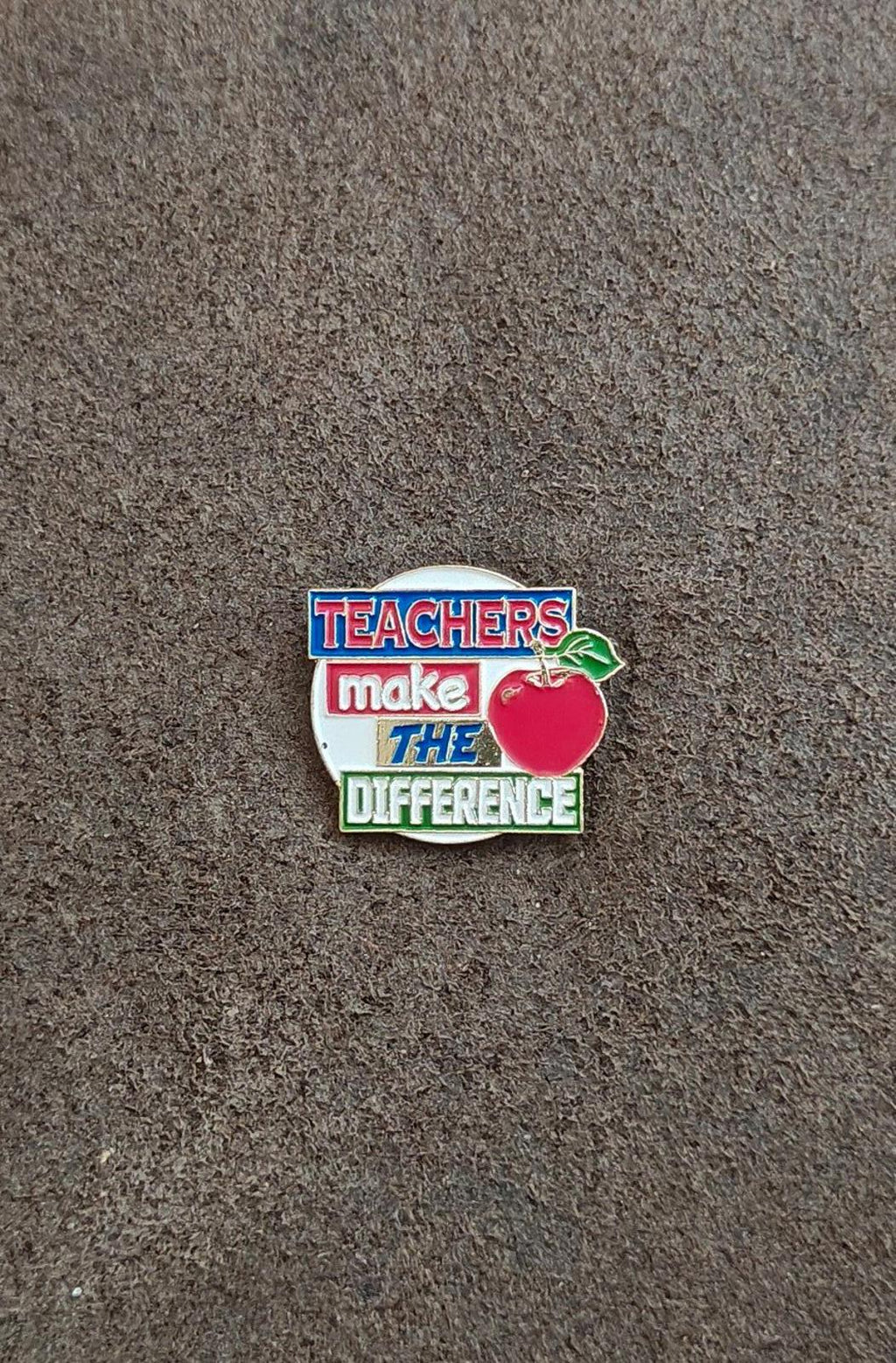 Small enamel teacher pin on gray background with red apple and green leaf