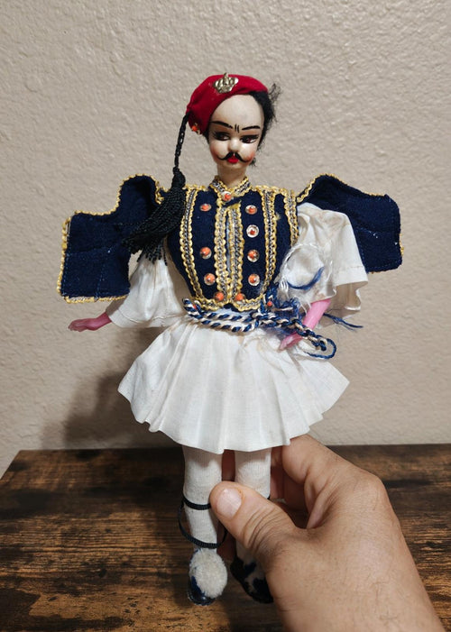 Greek folk male doll with red hat, navy vest, gold trim, white skirt, striped stockings