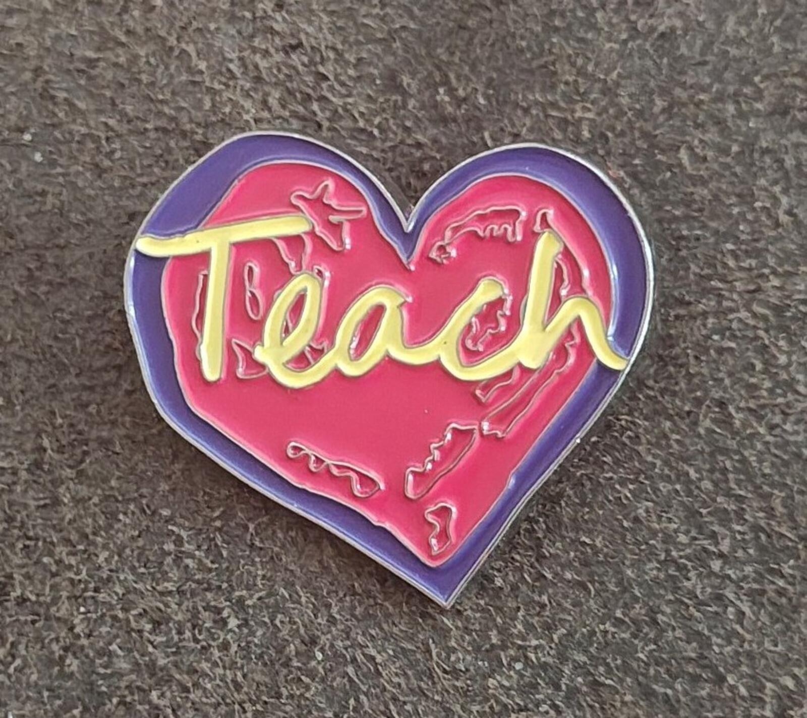 Enamel heart pin showing red “Teach” in yellow-and-purple enamel on a purple border.