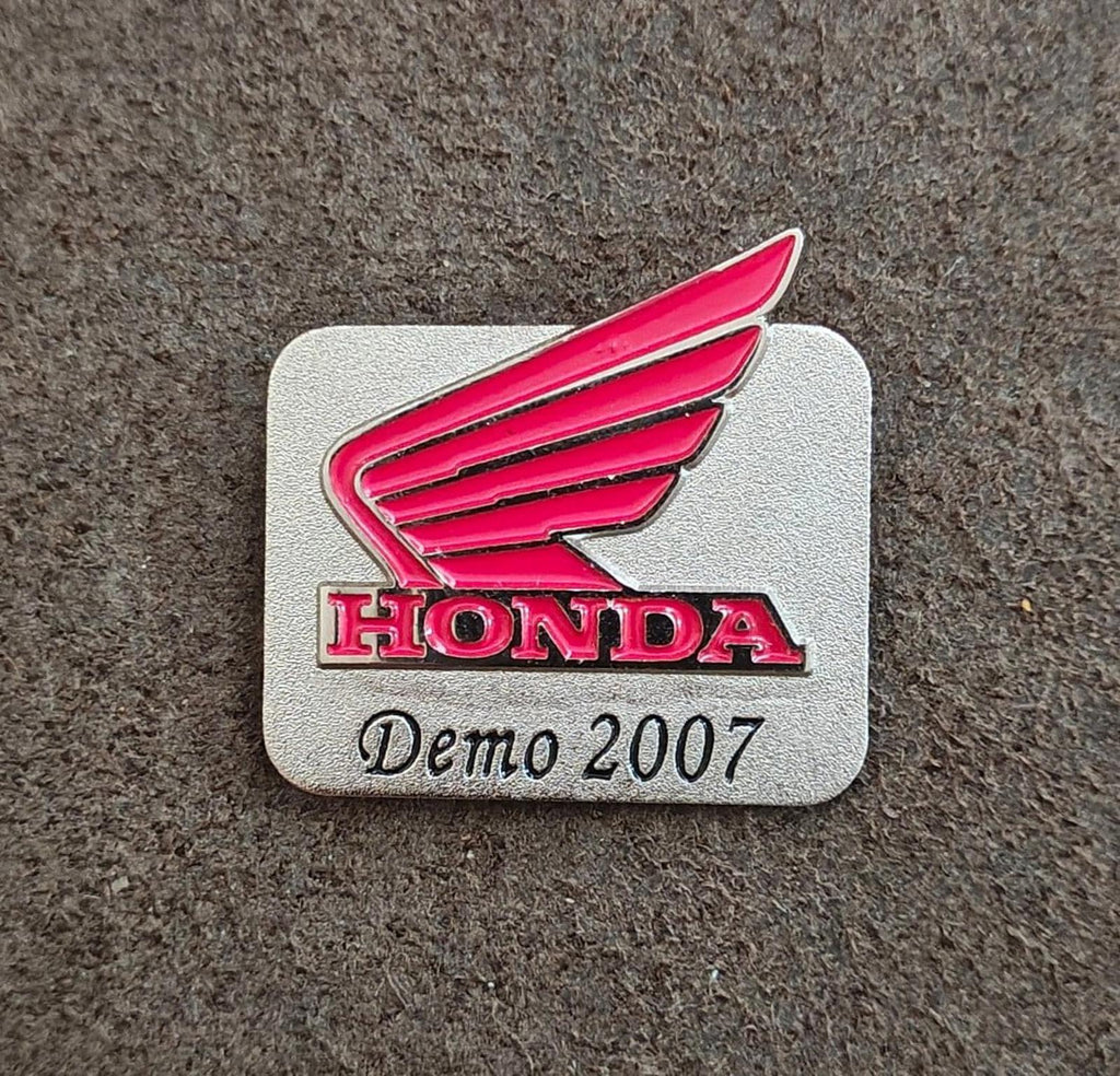Silver-tone Honda Demo 2007 enamel pin on gray surface with red wings and HONDA