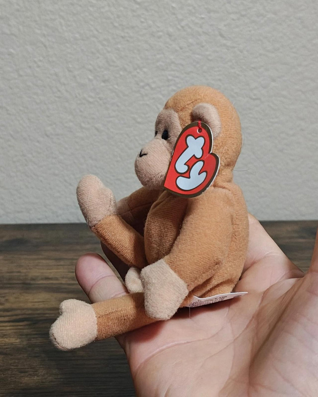 Brown Ty plush monkey in profile with heart tag, held in open hands