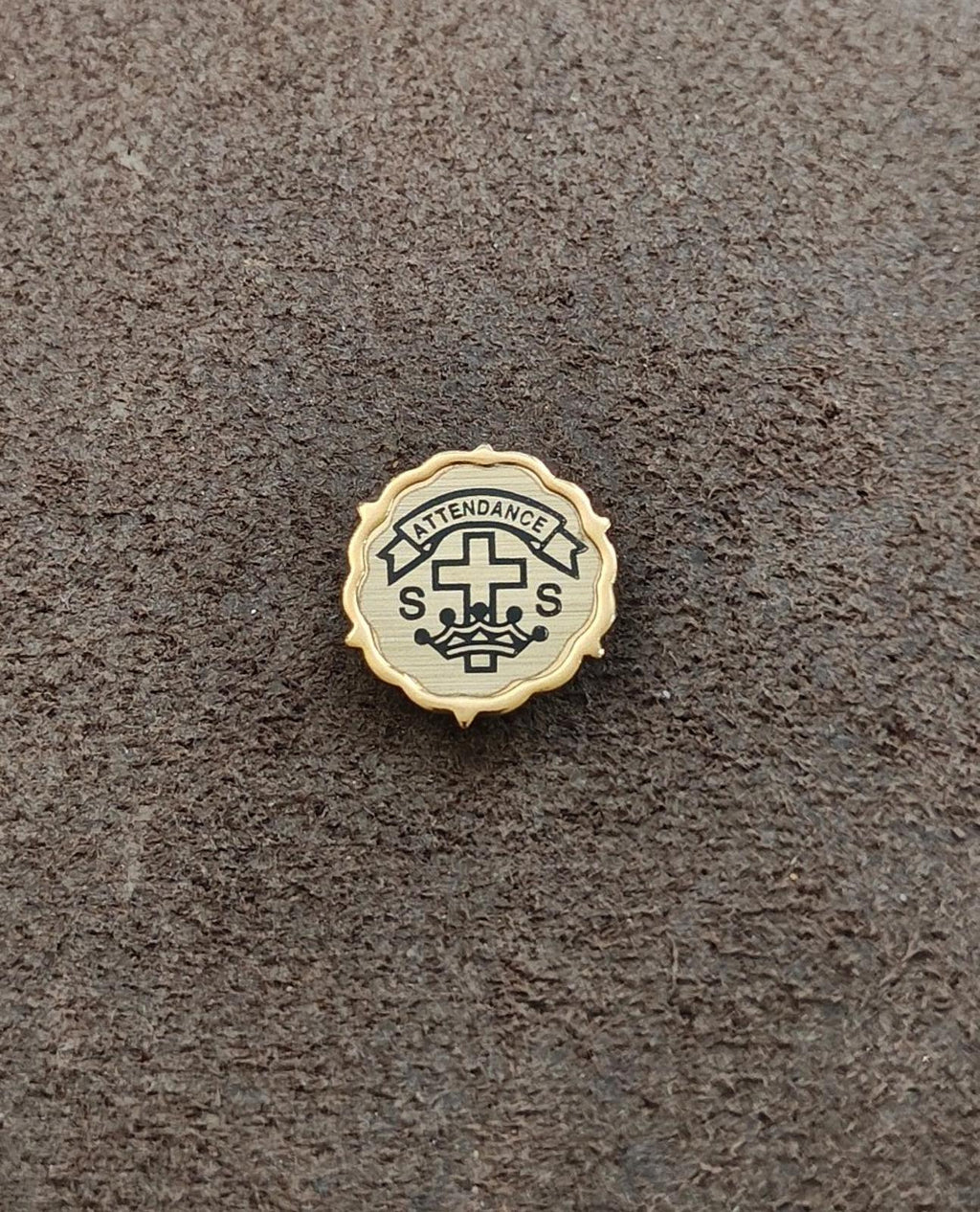 Gold-tone church attendance pin with cross symbol, banner text, and ornate border.