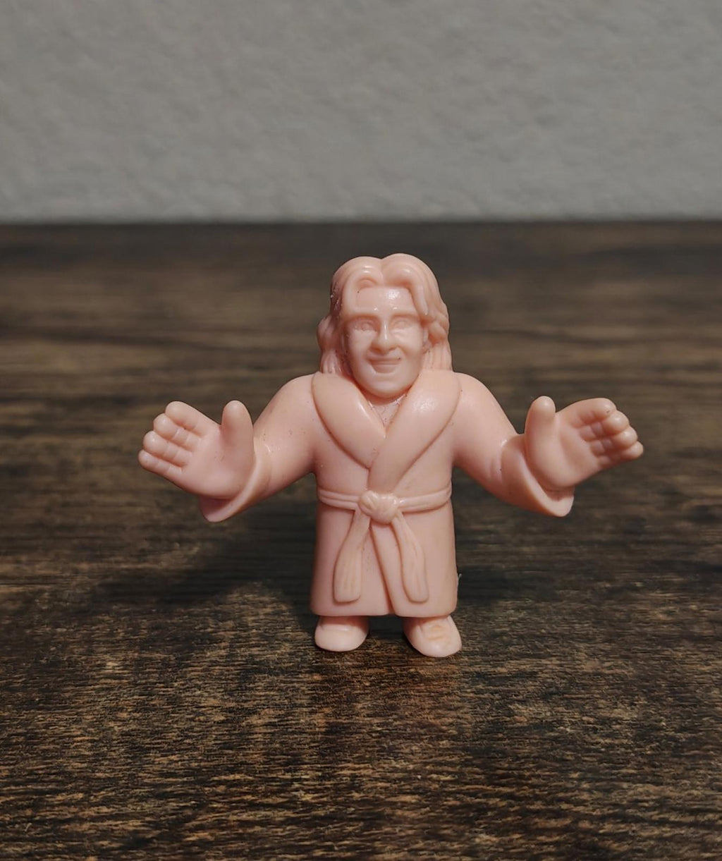 Pink bathrobe plastic wrestling mini figure standing on wood surface, arms open
