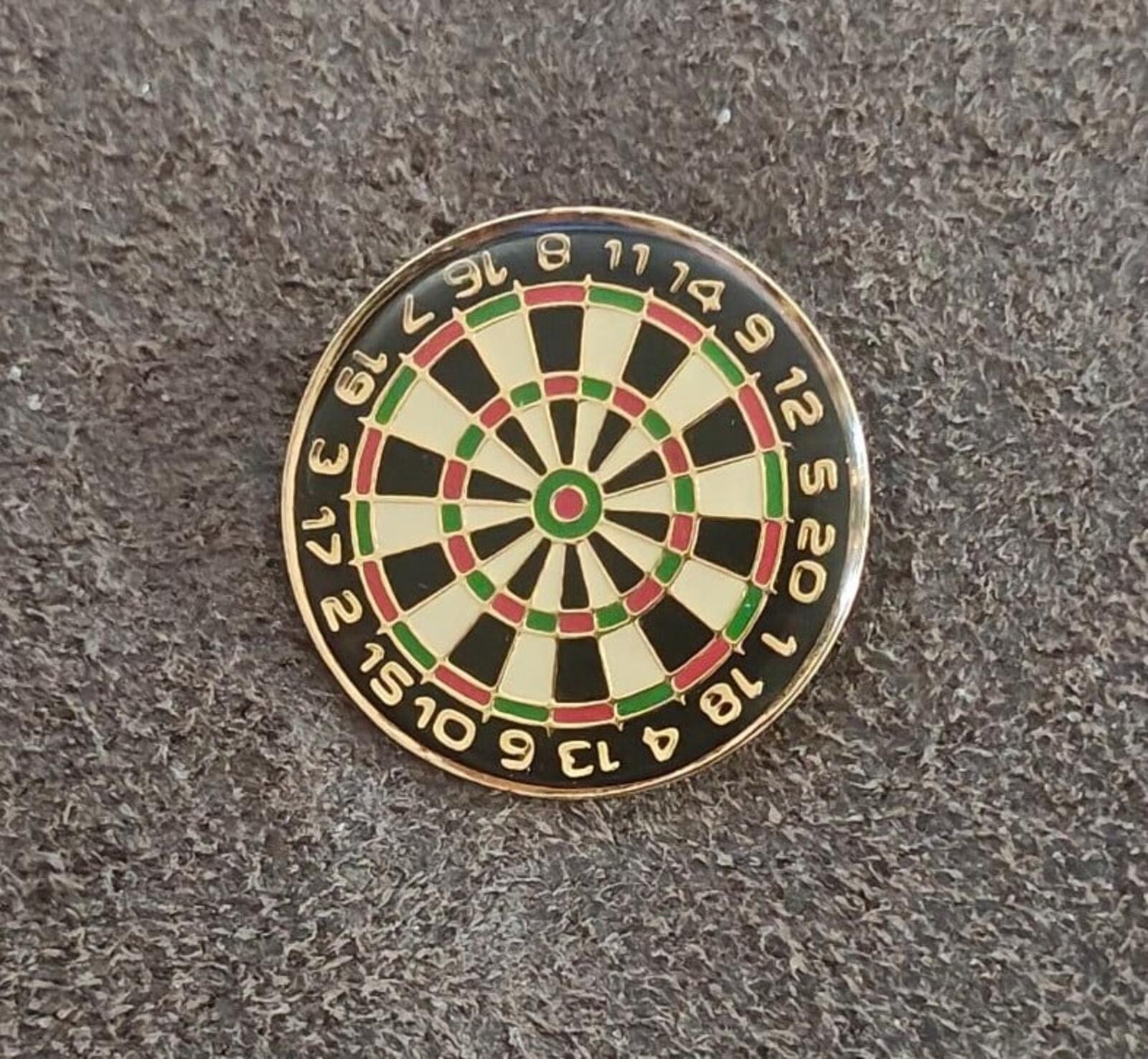 Round gold-tone dartboard enamel pin, dark and light segment spokes with green center circle.