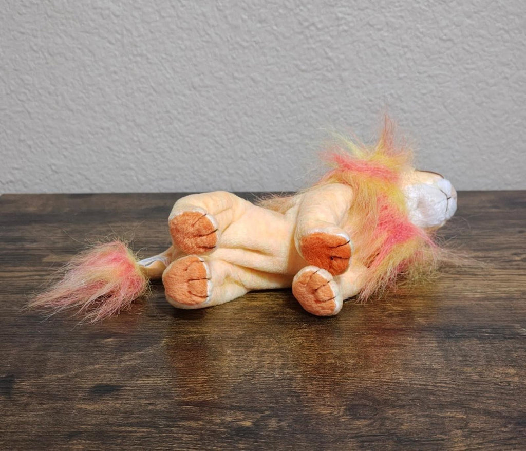 Rainbow-furred lion beanbag plush lying on its back with visible paws