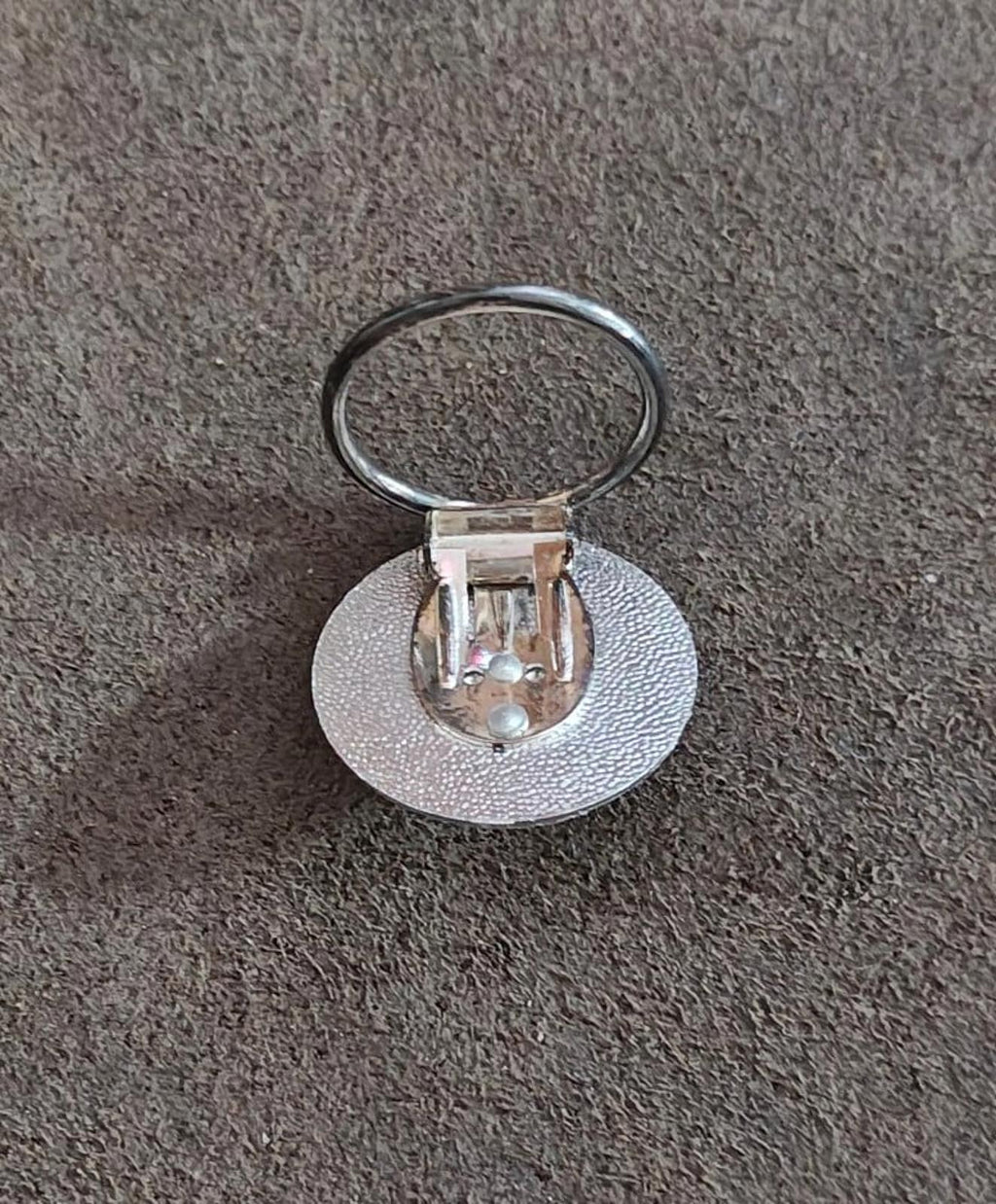 Back of round silver-tone scarf clip showing hinged pin and diamond-cut center