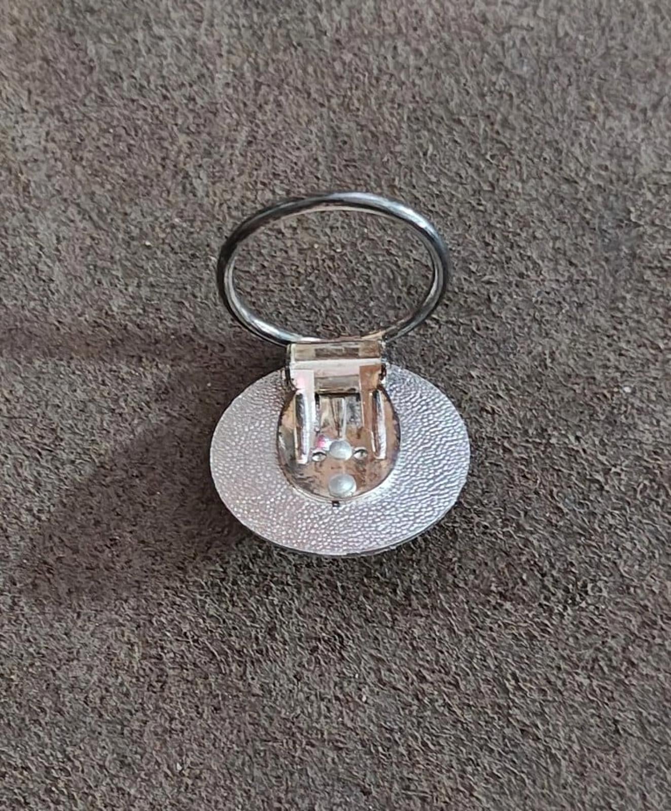 Back of round silver-tone scarf clip showing hinged pin and diamond-cut center