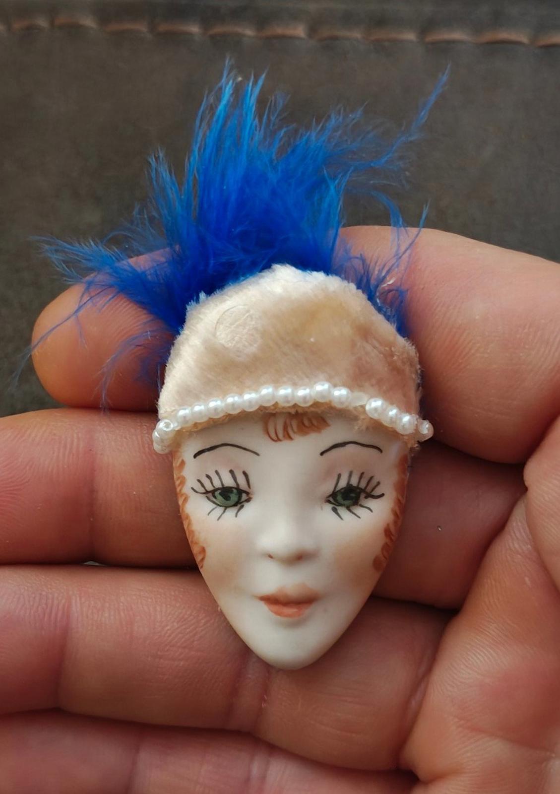 Doll face pin brooch with blue feather, cream headband, and faux pearl trim