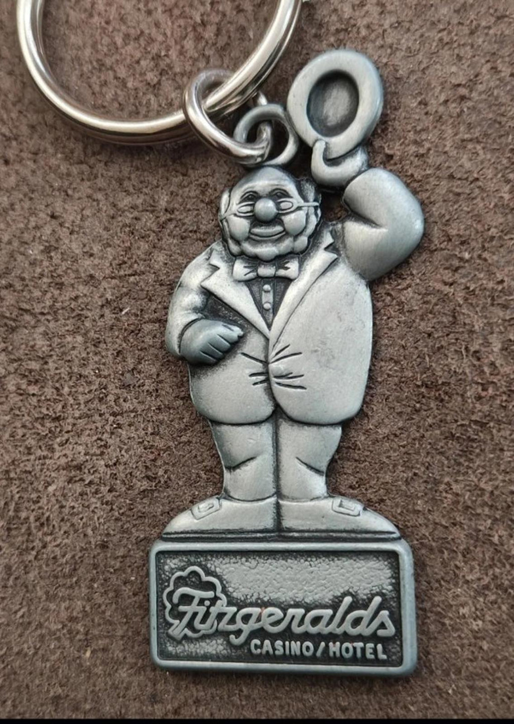 Silver keychain with teal cartoon man charm; raised hand and Fitzgeralds base text
