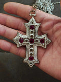 Silver tone cross pendant necklace with red rhinestone inlays on a handheld chain