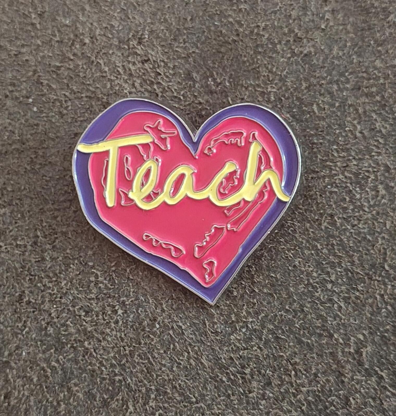 Enamel heart pin with purple outline, red “Teach” lettering, and yellow details.