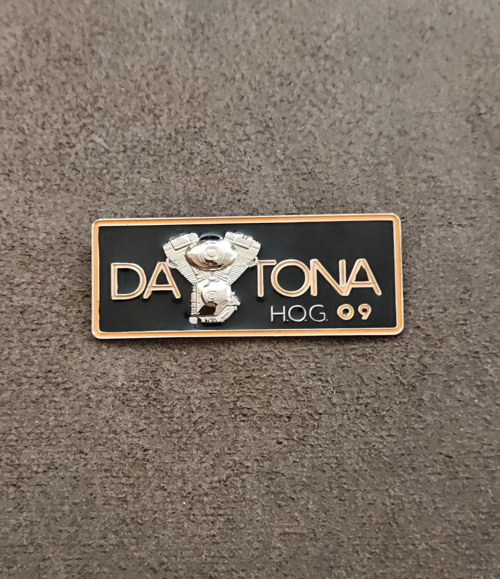 Black enamel Daytona H.O.G.09 pin with silver eagle badge and gold border on fabric.