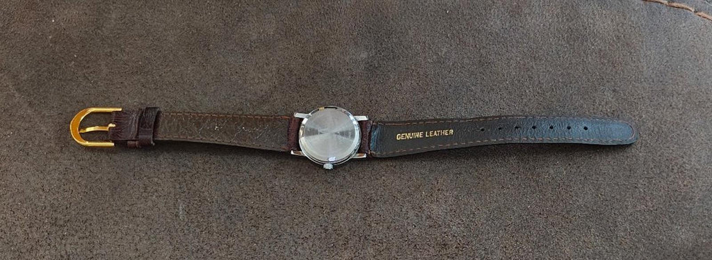 Brown leather wristwatch laid flat with round silver case and dark buckle