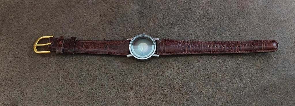 Brown leather wristwatch laid flat with small round case and gold-tone buckle