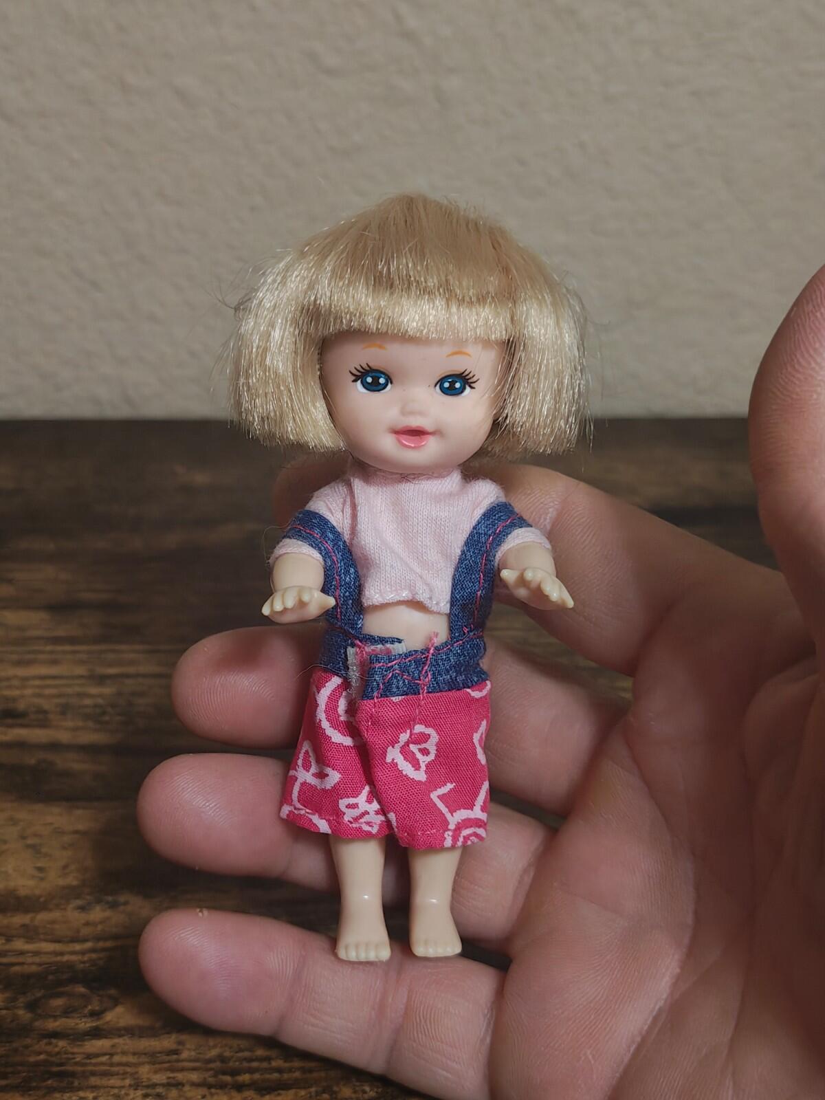 Mini girl doll with blonde bob hair, blue top, pink patterned shorts, vinyl face