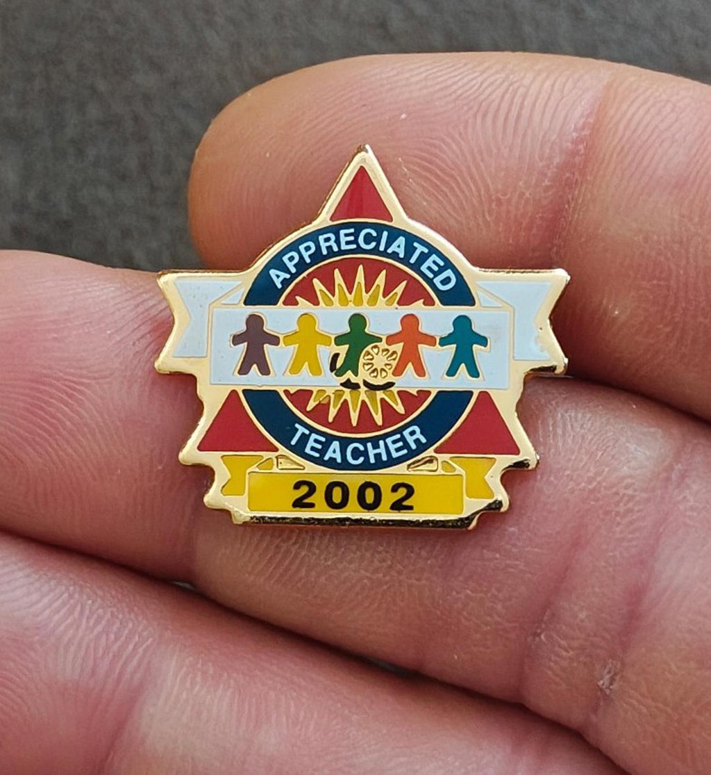 Teacher enamel pin close-up: gold-tone, blue “Appreciated Teacher” text and “2002”