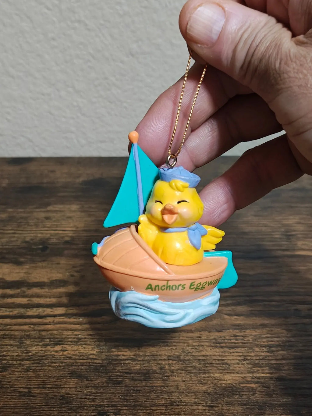Hand holding yellow chick sailboat ornament with gold chain and orange top bead