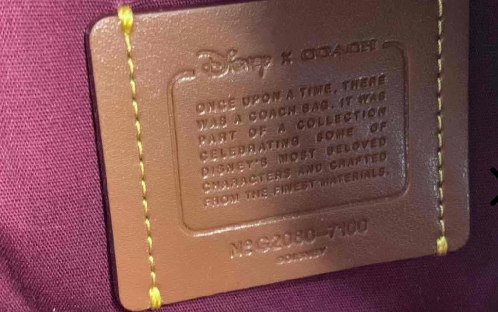 Coach leather care label with debossed text and yellow stitch, close-up