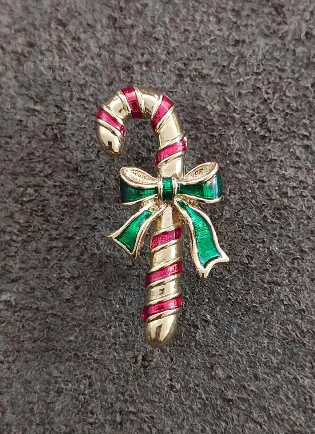 Candy cane enamel pin with striped red enamel, green ribbon bow, and gold-tone base