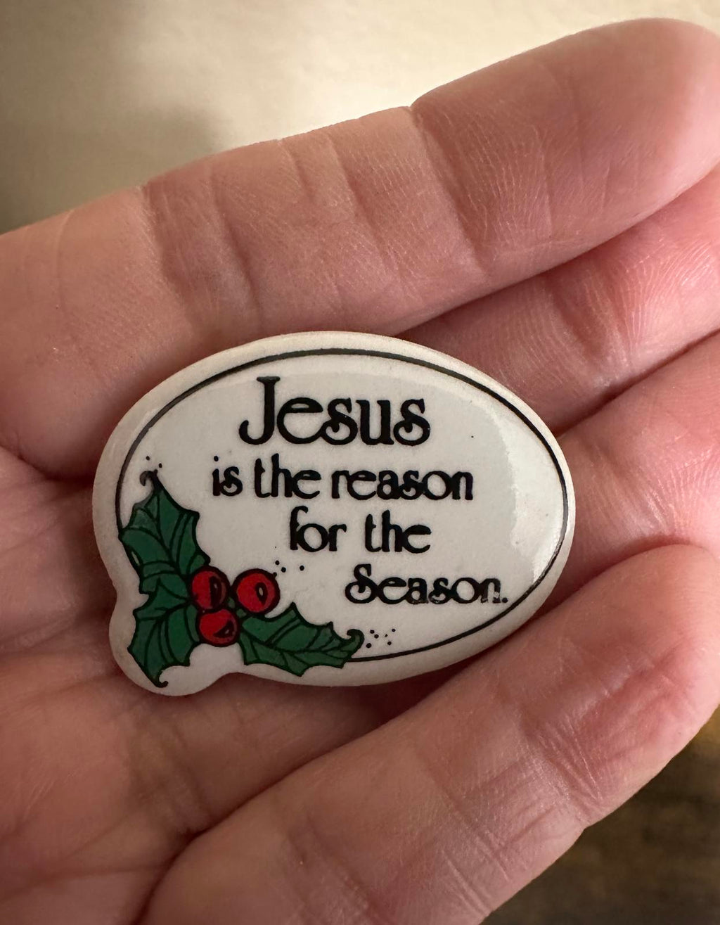 Jesus holiday lapel pin in hand showing oval white design and holly berries