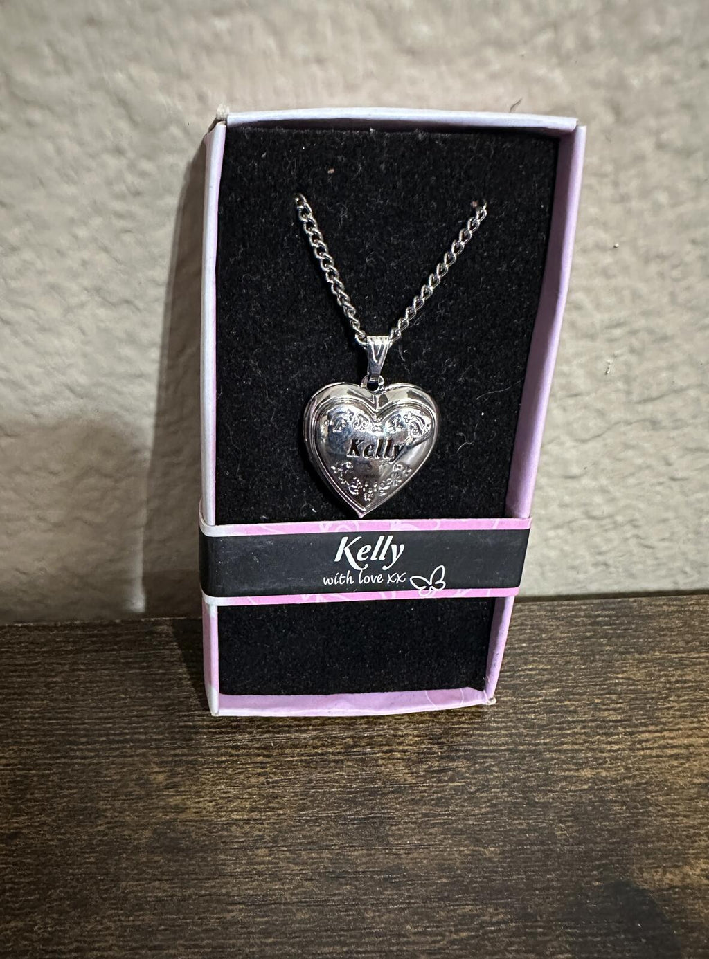 Silver heart locket necklace with engraved Kelly pendant in gift box on wood surface