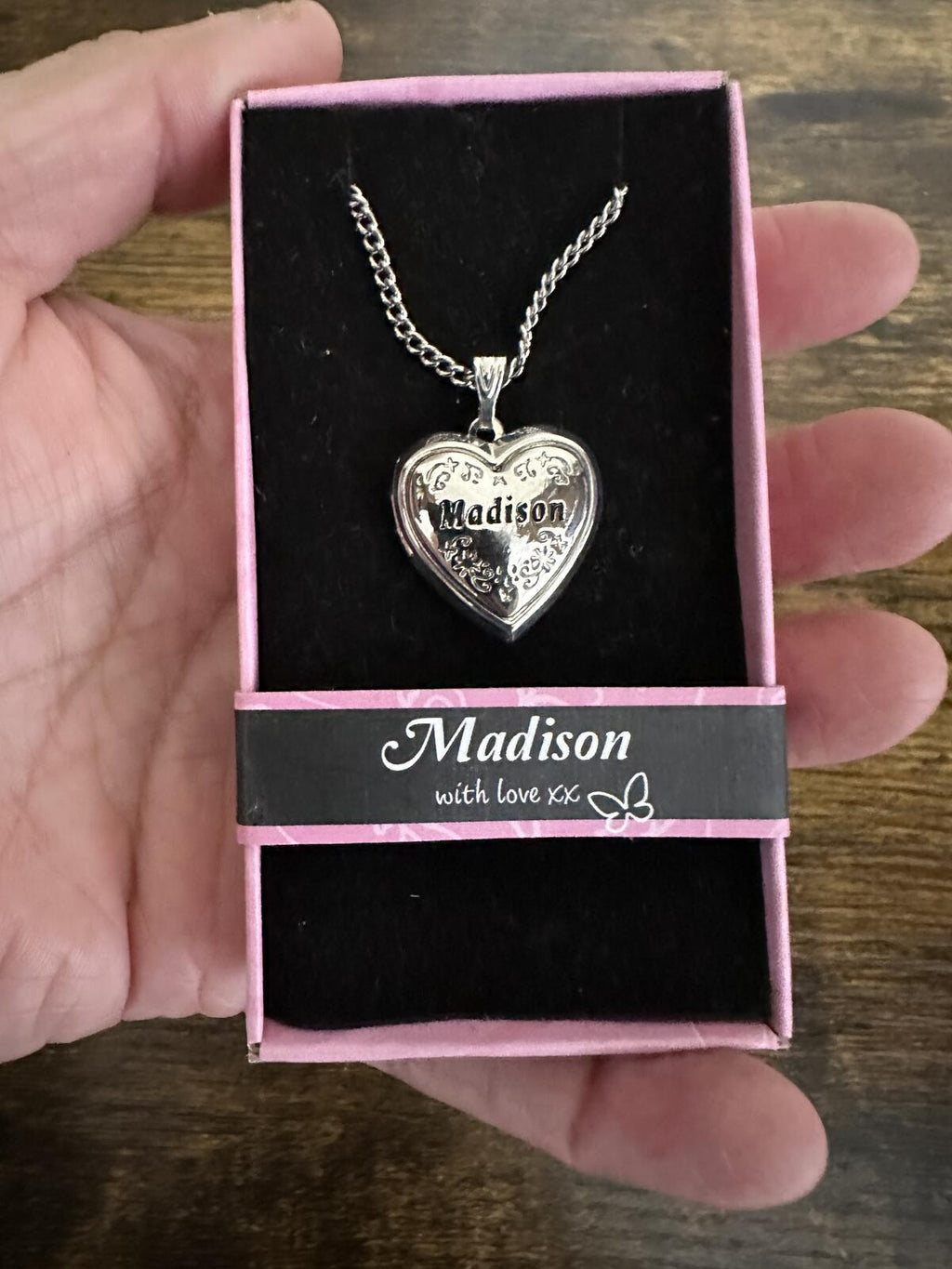 Silver-tone heart locket necklace in box, held in hand, with engraved heart charm