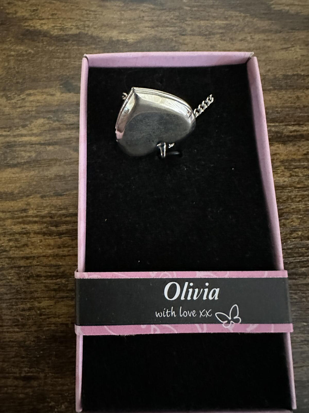Silver-tone heart locket necklace shown from side with engraved Olivia