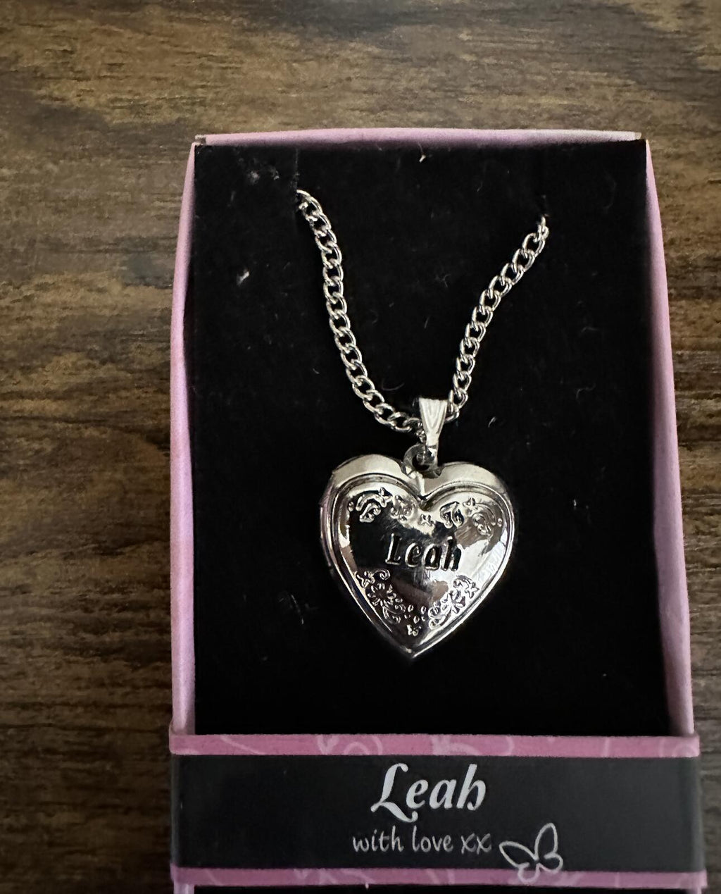 Silver-tone heart locket necklace with engraved 'Leah' heart pendant in pink gift box.