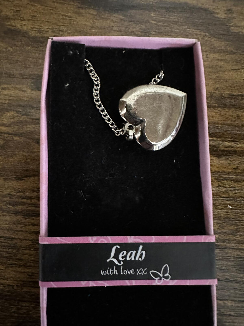 Silver-tone heart locket necklace with chain and heart pendant back, shown in box.