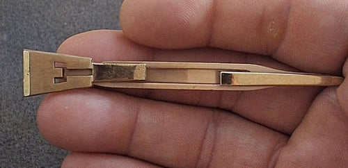 Gold-tone tie clip bar with letter E monogram and sword-style frame, held in hand