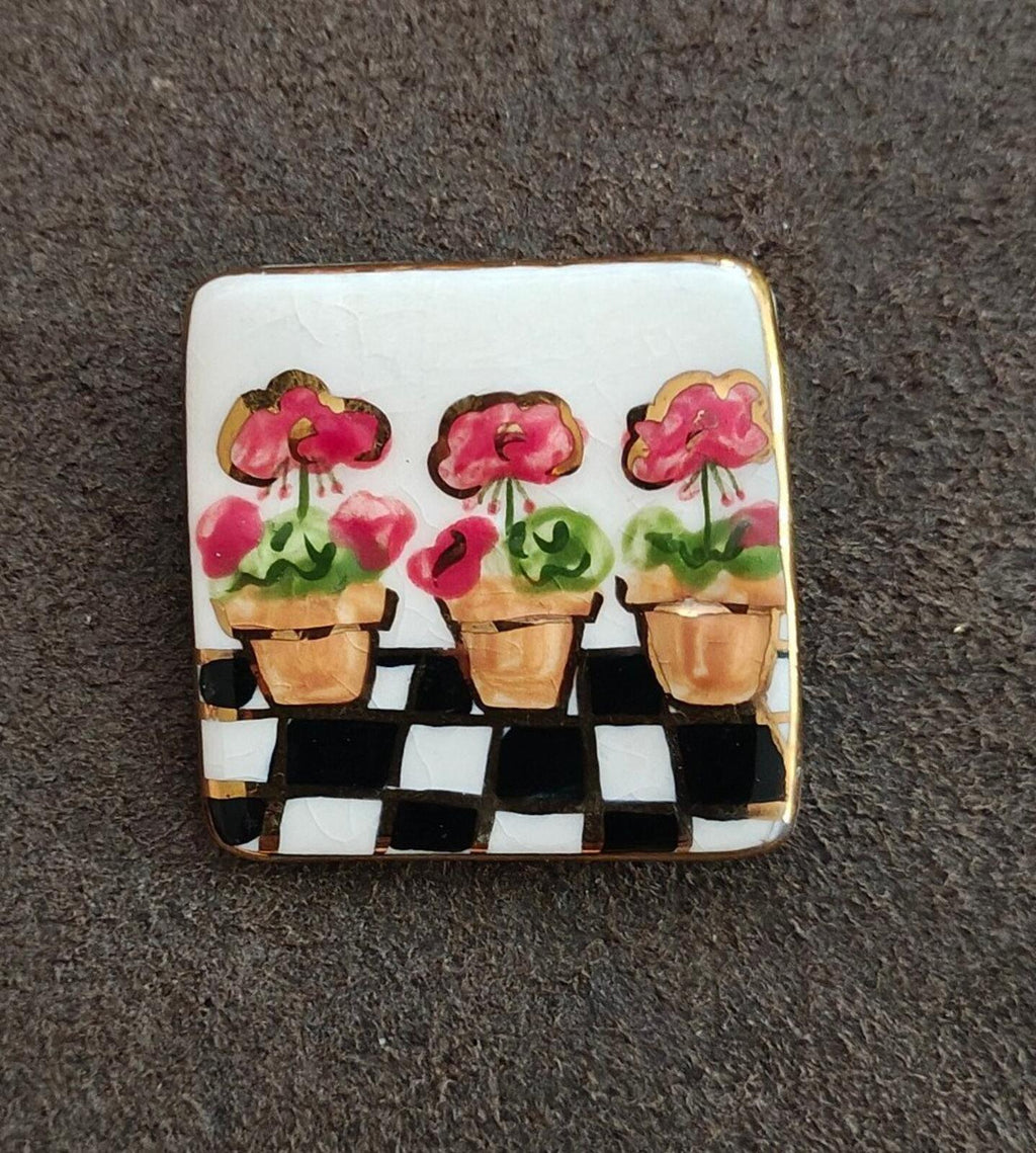 Square glazed ceramic brooch with pink floral heads in three pots and checker band below