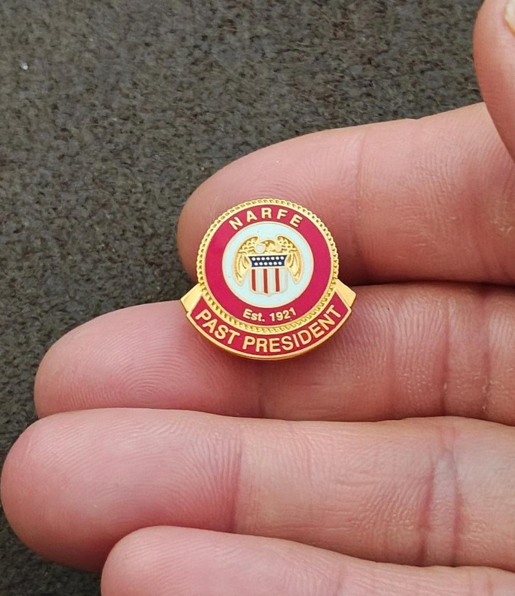 Small red and gold association pin in hand, reading “PAST PRESIDENT”
