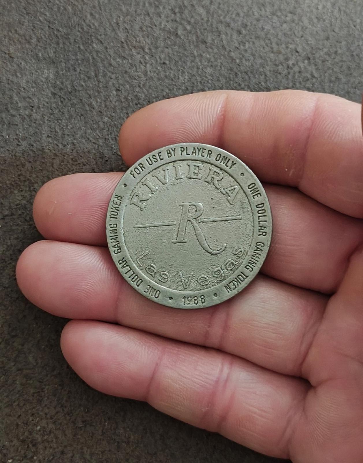Silver one-dollar gaming token held in hand with Riviera logo and one dollar ring text