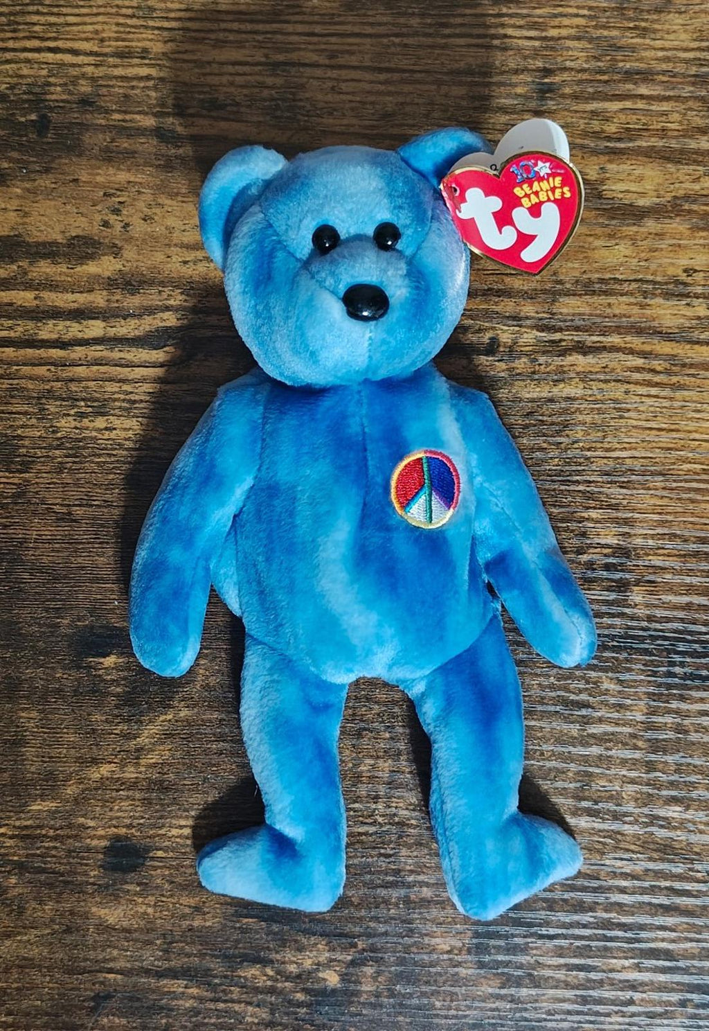 Blue bear plush standing on wooden surface with peace symbol patch and Ty heart tag
