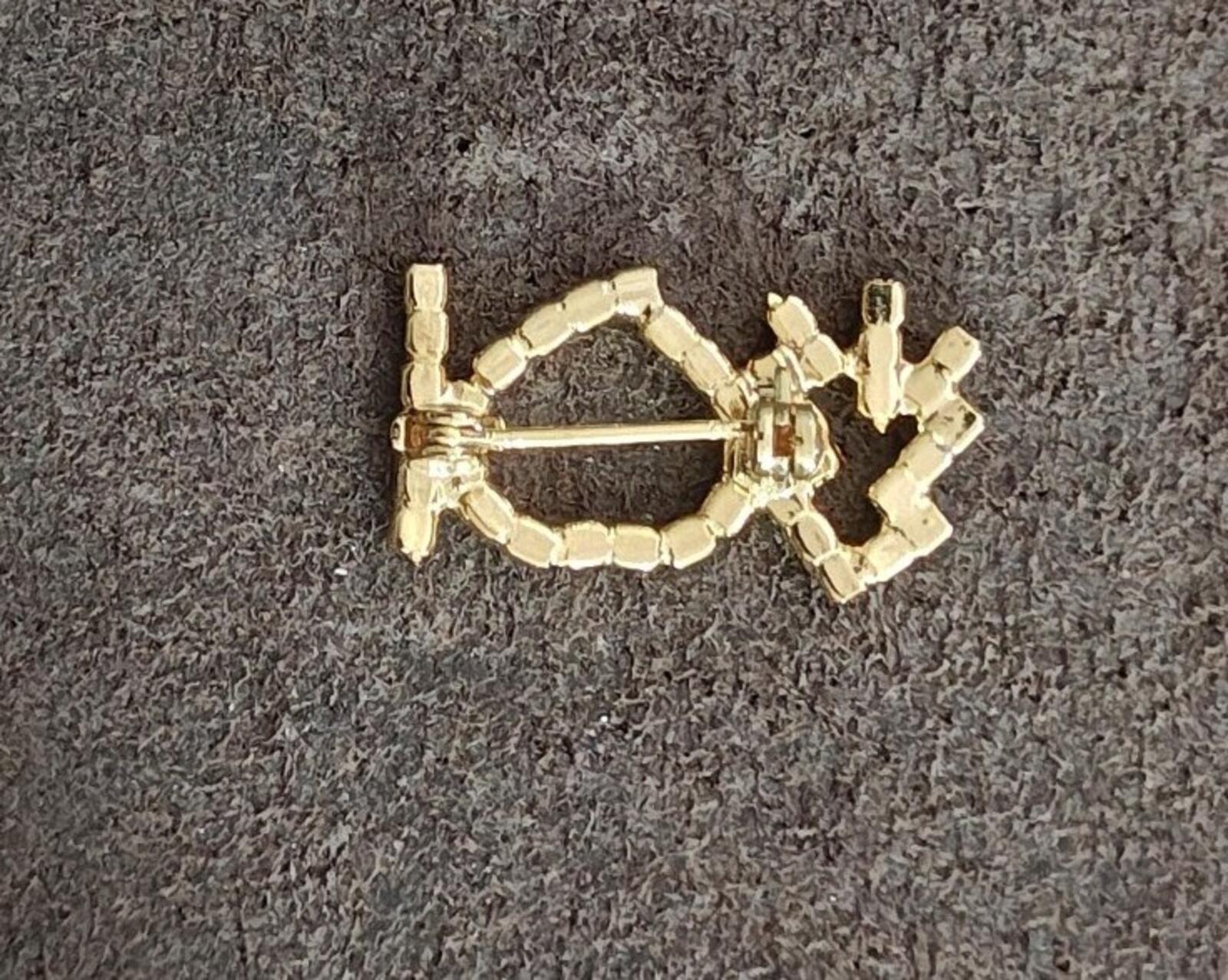 Gold-tone brooch clasp and pin mechanism with rhinestone settings on dark fabric