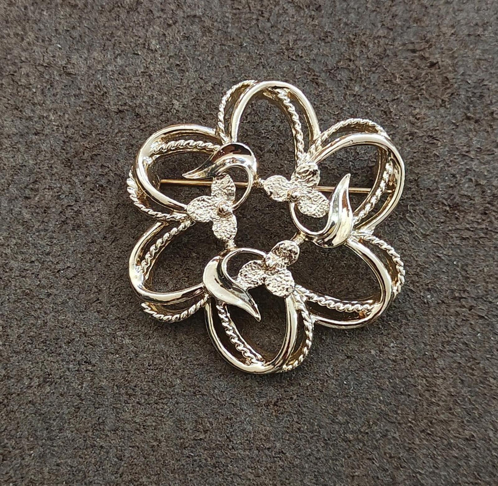 Gold-tone flower brooch with scalloped, ribbon-like petal edges and filigree details