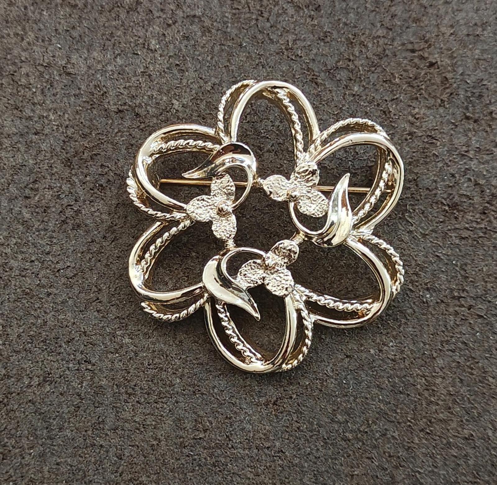 Gold-tone flower brooch with scalloped, ribbon-like petal edges and filigree details