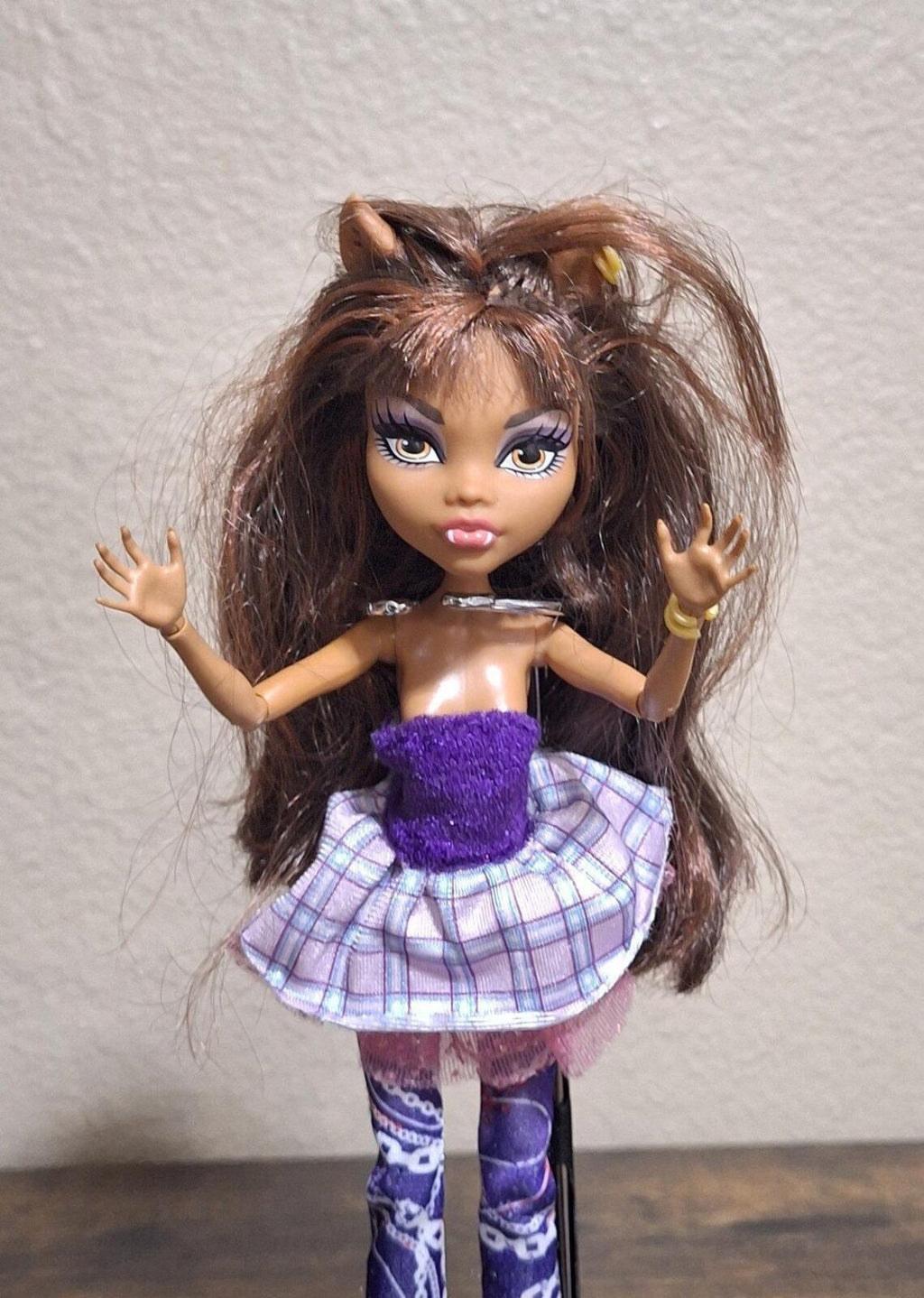 Fashion doll with arms raised, purple glitter tube top and plaid ruffled skirt