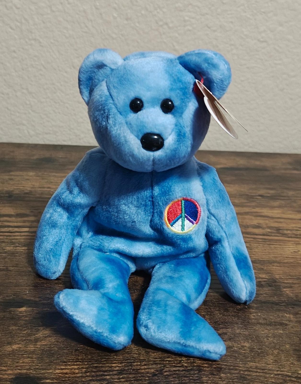 Blue bear plush kneeling pose with peace symbol patch on chest and hanging tag