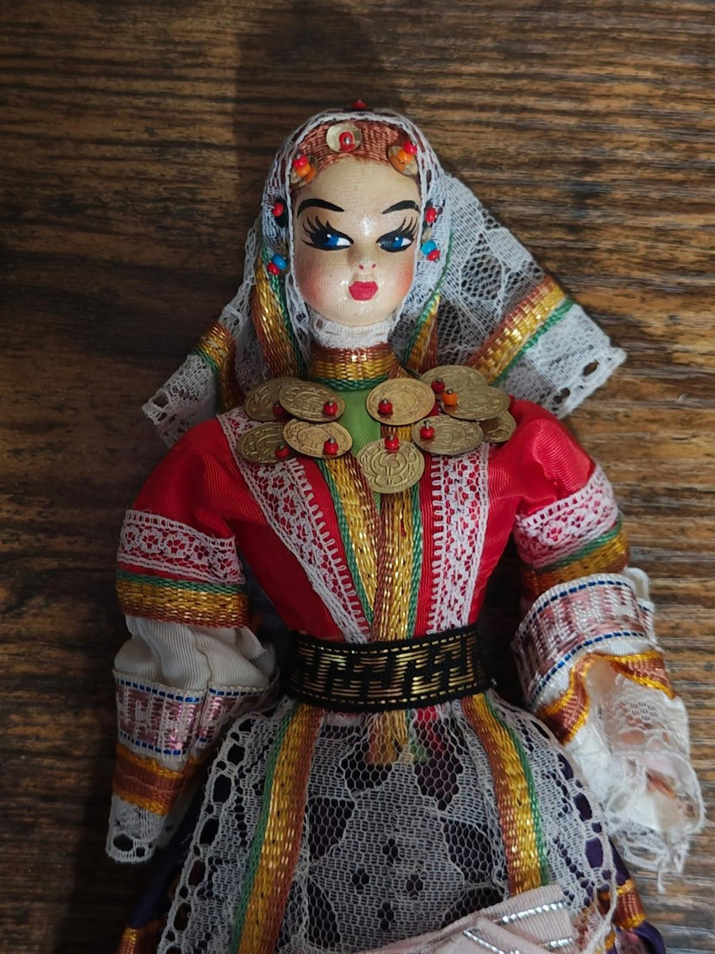 Female folk doll close-up with red dress, gold coin chest, multicolor trim, and lace cap