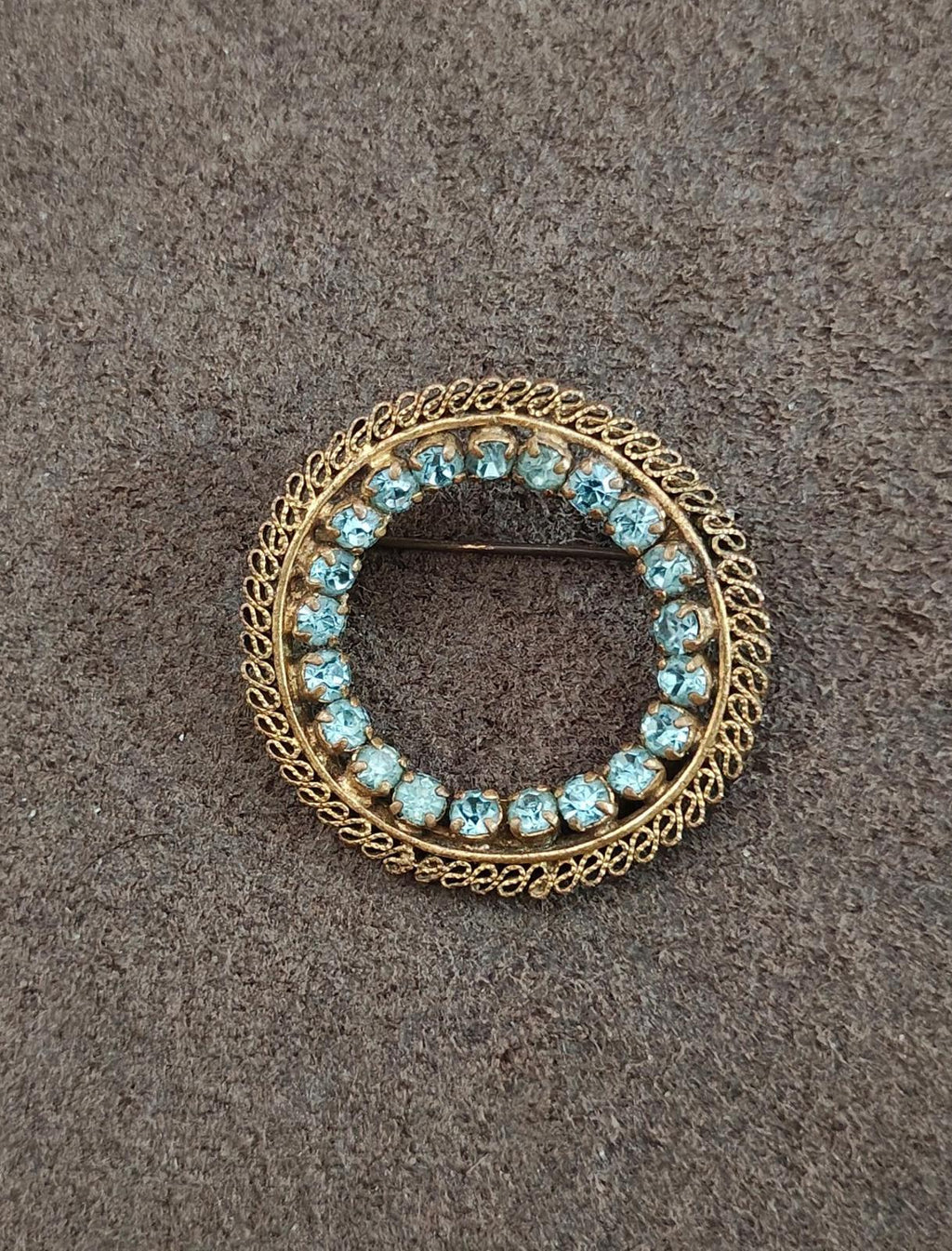 Round gold-tone brooch with bright blue stones and decorative filigree rim