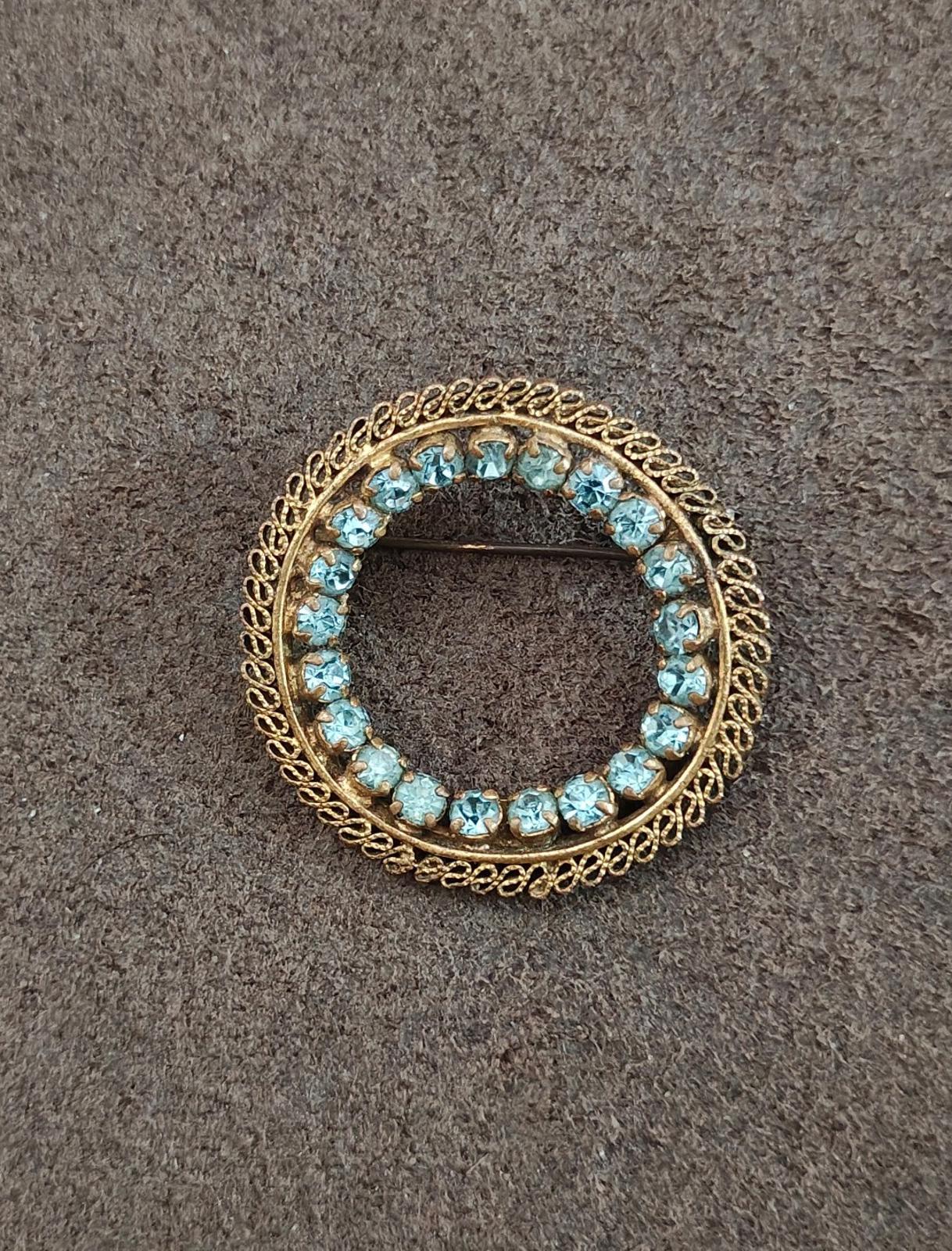 Round gold-tone brooch with bright blue stones and decorative filigree rim