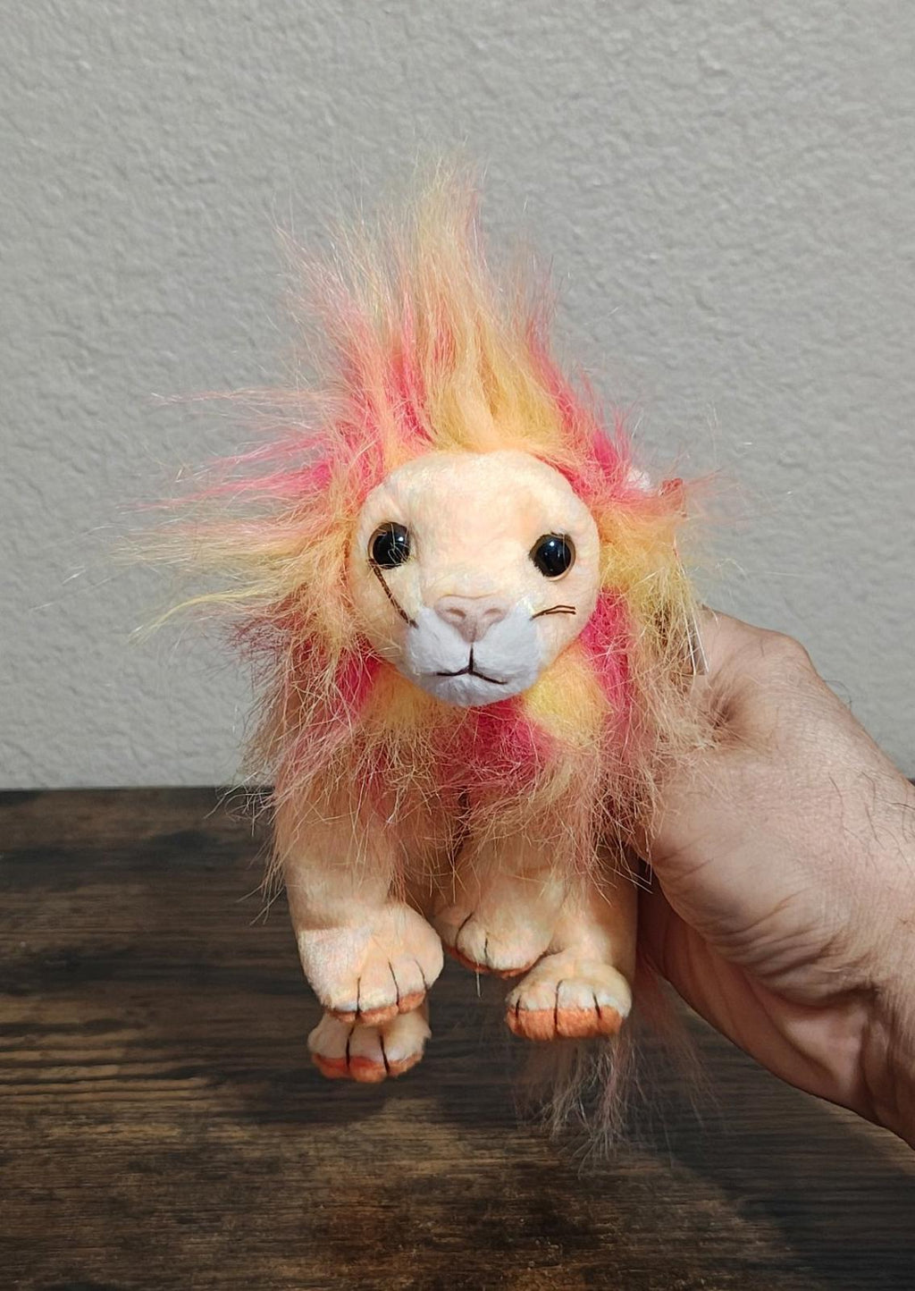 Rainbow-furred lion beanbag plush with big round eyes, held in a hand